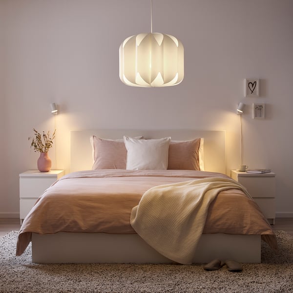 Cosy bedroom: central bed, warm lights, pink pillows, decor on nightstands, soft walls, rug, slippers, pendant light.