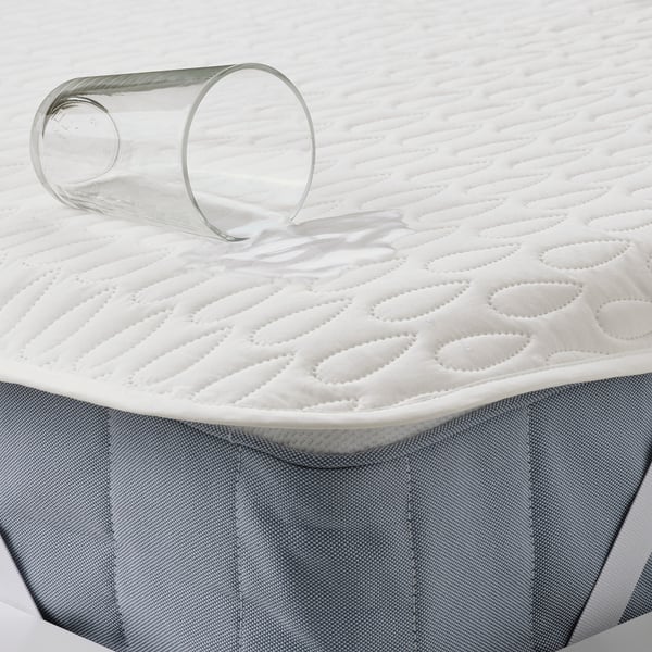 A rolled-up white waterproof mattress protector with a glass of water on top, demonstrating its spill-proof feature.