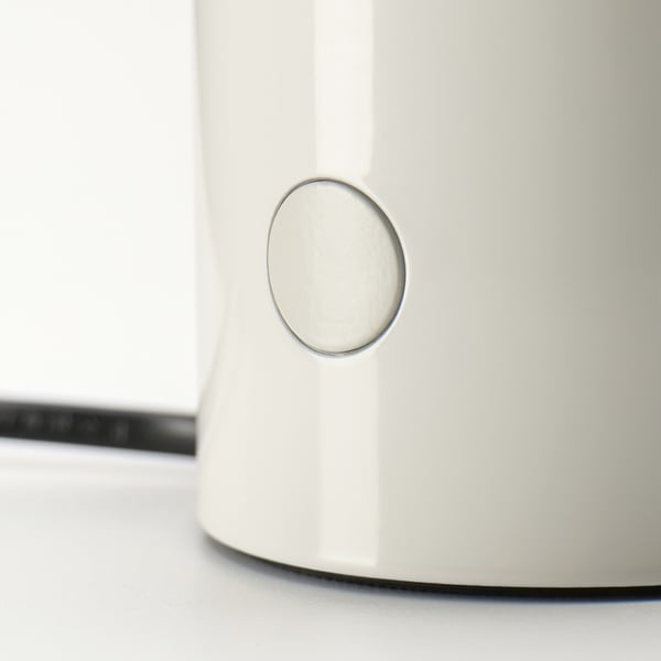 Sleek modern lamp with smooth white finish and metallic button on side, resting on a light surface.