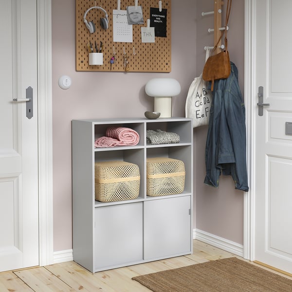 Modern grey storage cabinet with open shelves, closed cabinets, and a lamp. Pegboard and coat rack nearby for additional storage.