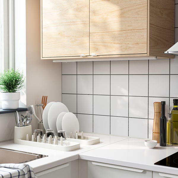 Modern kitchen with wooden cabinets, white counters, STÄMLING dish drainer, plant, oil bottles.
