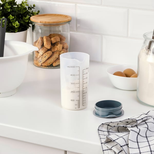 A kitchen counter with a measurement shaker, cookie jar, mixing bowl, and other baking items.