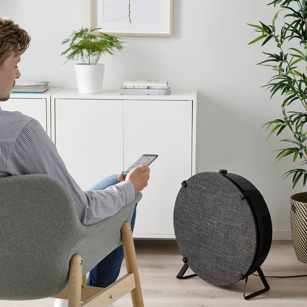 Man sitting in living room, controlling ikea STARKVIND air purifier via smartphone.