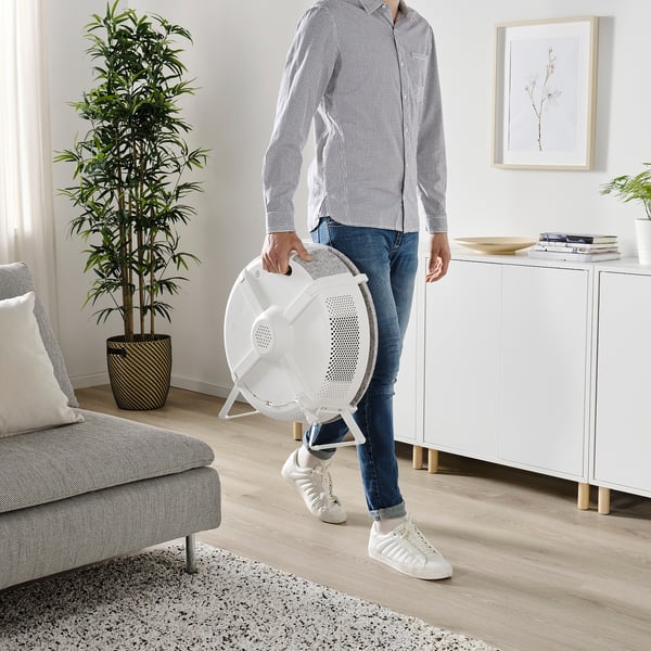 Person holding a white STARKVIND air purifier in a living room, showcasing its portable design with an integrated handle.