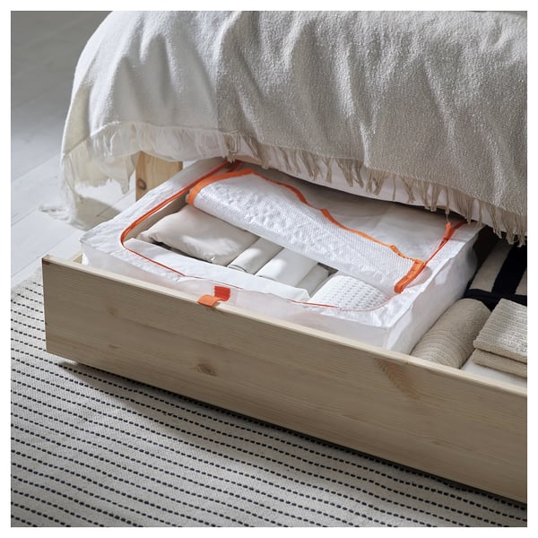Open wooden drawer under bed showing neatly rolled white and orange items with cotton covers and dividers.