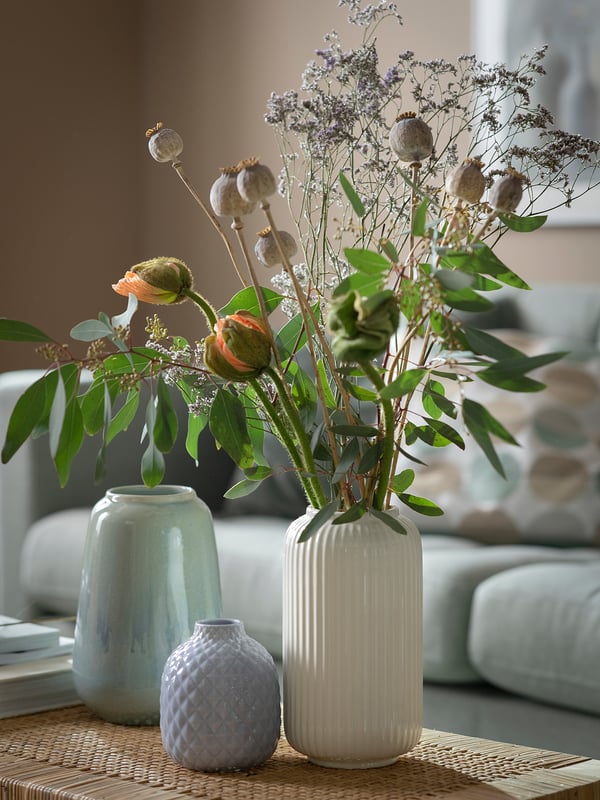 Three vases on a table. Left: light blue, smooth. Middle: light purple, textured. Right: white, ribbed, holds flowers.