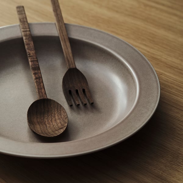 Dark wooden salad servers rest in a matching bowl, showcasing sleek, minimalist design and high-quality craftsmanship.