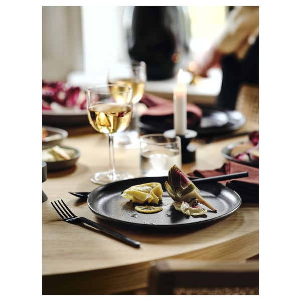 Dining table set with dark cutlery, artichoke, lemon, wine glass, candles.