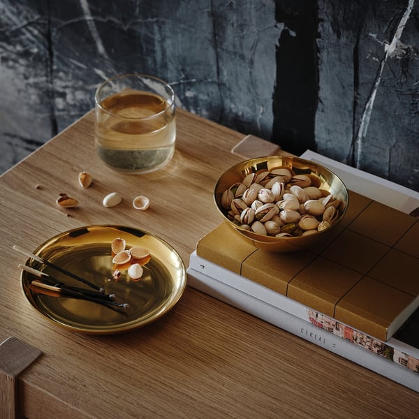 Small brass-colored bowl and dish on a table with pistachios, matches, and a drink. Used for storage and decoration.
