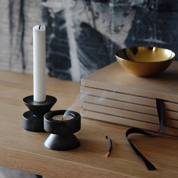 Black metal candlesticks on wooden table, one reversible for tall and tealights, gold bowl nearby.