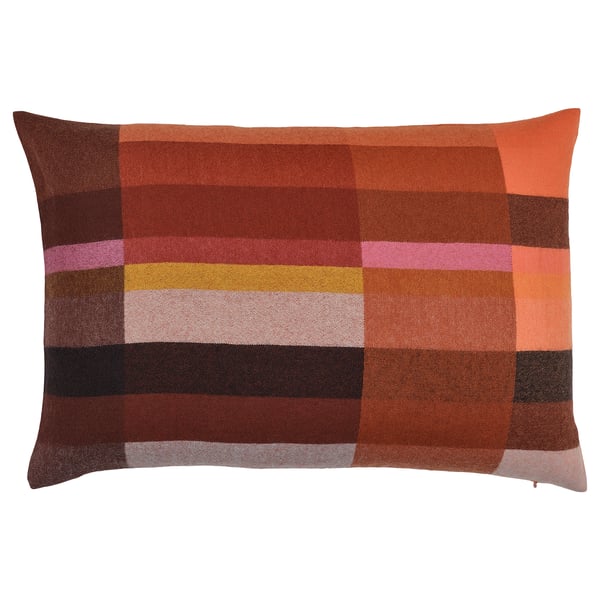 A rectangular STOCKHOLM 2025 wool cushion in warm reds and bright pink, showing a geometric pattern designed by paulin machado.