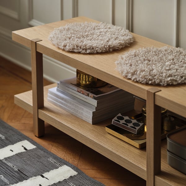 Light wood bench with soft rugs, books, and small items on a striped rug.