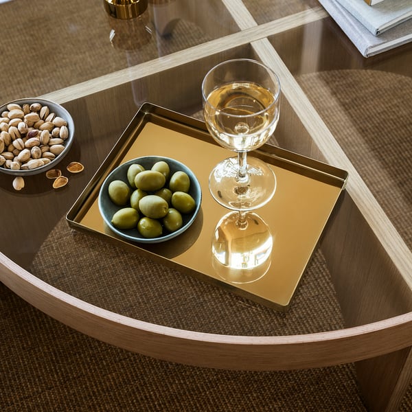 A stylish tray holds a glass of wine and a bowl of olives on a modern table.