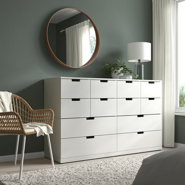 Modern bedroom with white STOCKHOLM dresser, mirror, wicker chair, lamp, and plant.