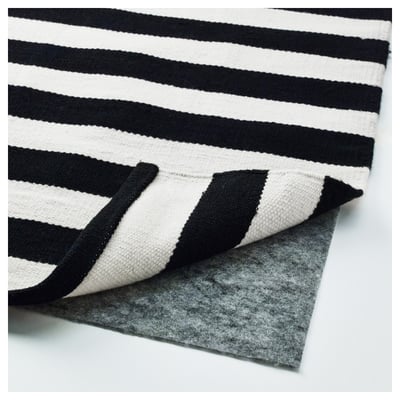 Black-and-white striped rug with reverse pattern, likely handwoven, displayed with an anti-slip underlay.