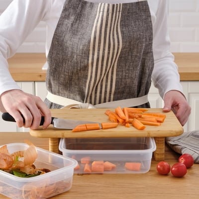 Person prepares food on STOLTHET cutting board with built-in containers for efficient chopping and storage.