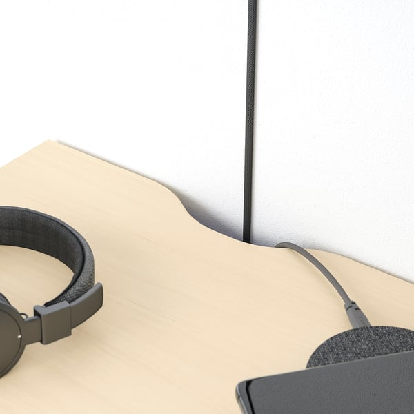 Black headphones rest on a beige surface beside a grey wall-mounted table with a cut-out for cables.