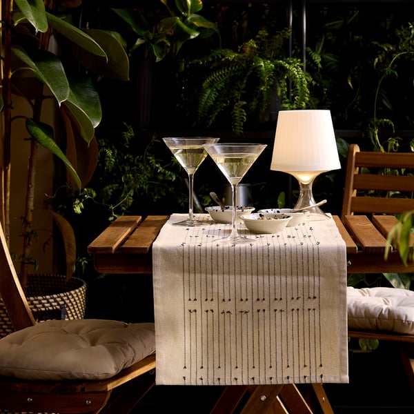 Indoor patio with wooden table, two martini glasses in STORSINT clear crystalline next to a small lamp, bowls, and cushioned chairs.