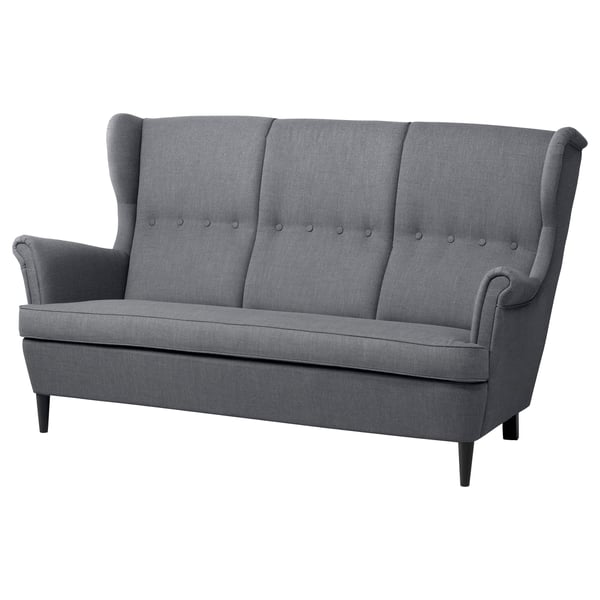 A grey IKEA STRANDMON 3-seat sofa with high, winged backrests, button-tufted cushions, and dark wooden legs.