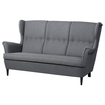 A grey IKEA STRANDMON 3-seat sofa with high, winged backrests, button-tufted cushions, and dark wooden legs.