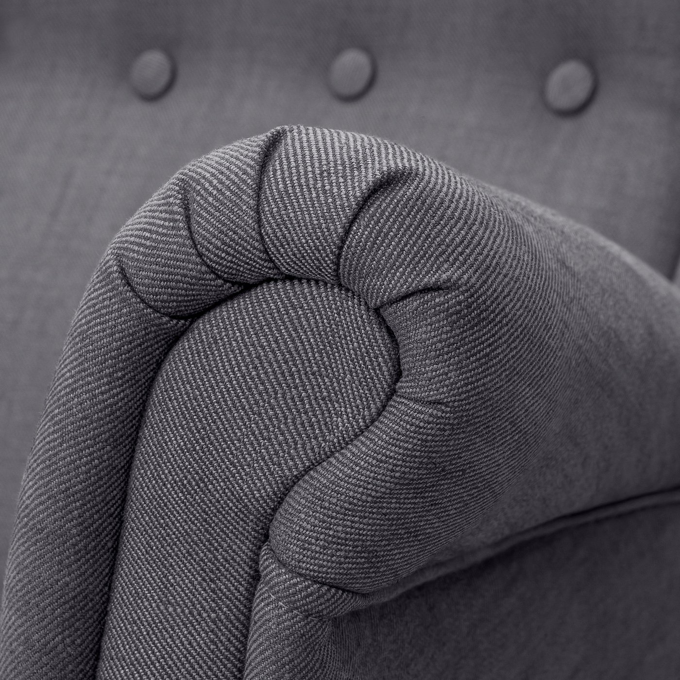 Close-up of high-quality, grey tweed fabric on a upholstered sofa armrest, showcasing its texture and detail.