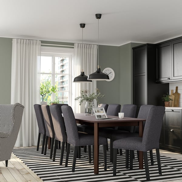 Modern dining room with extendable table, grey chairs, striped rug, large window, and kitchen cabinets.
