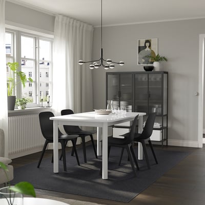 Modern dining room with extendable table, black chairs, large window, grey walls.