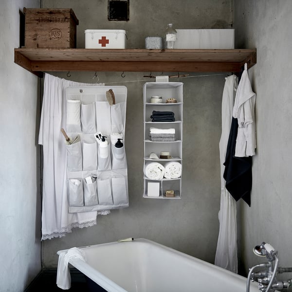 Bathroom with white bathtub, organiser with clothes, accessories, and first-aid box, white curtain.