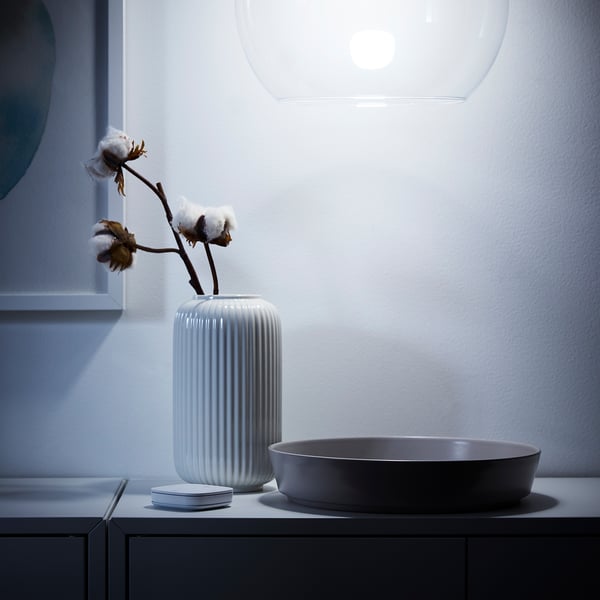 Modern bathroom with white ribbed vase holding cotton plant, round grey sink, and stylish pendant light overhead.
