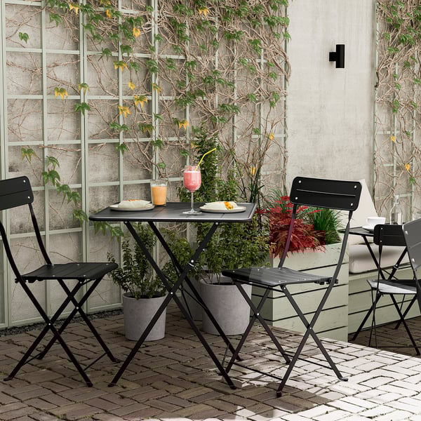 Black metal outdoor table set with two chairs, flowers, glasses, and plates. Perfect for small spaces.