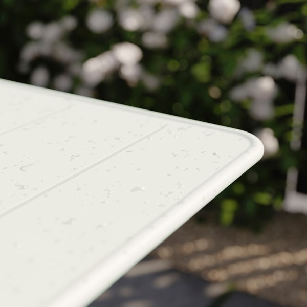 White SUNDSÖ table edge outdoors with water drops. Made of steel, powder-coated. Modern foldable design for balconies.