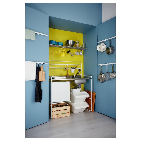 Bright kitchen with blue walls, yellow backsplash, hanging pots, wooden stool, sink, and storage units.