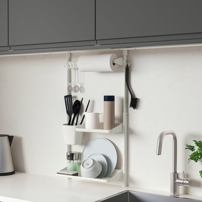 Modern kitchen with SUNNERSTA white shelf holding mugs, plates, and utensils. Compact, fits under cabinets, made of polypropylene.