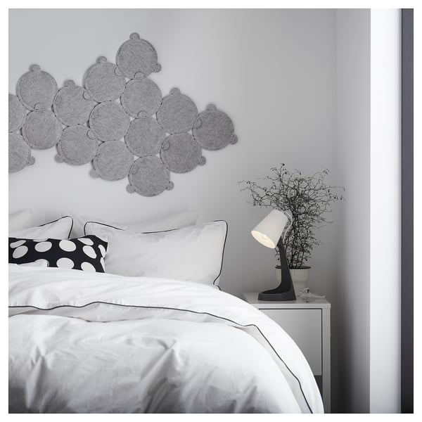 Modern minimalist bedroom with white bedding, black lamp on white bedside table, and grey circular wall decor.