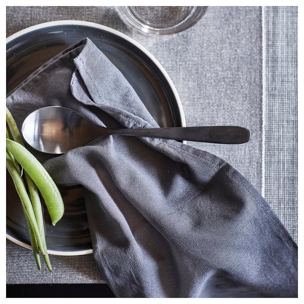 Dark grey napkin with green beans and metal spoon on dark plate. Simple, elegant table setting.