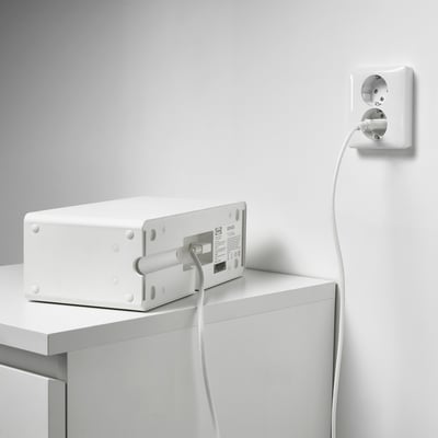 White power supply cable plugged into wall socket, extending to white speaker on table.