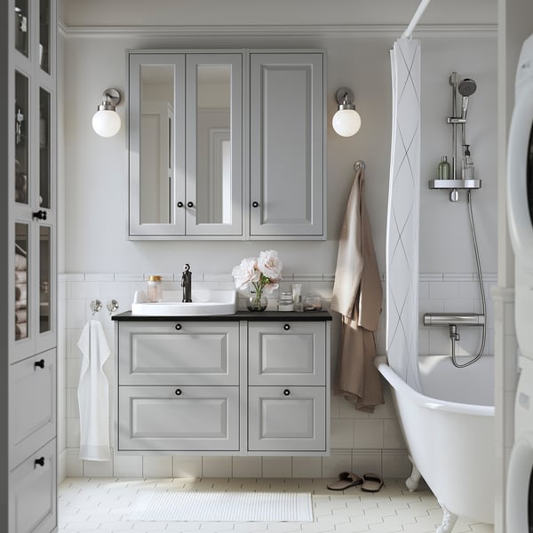 Modern grey bathroom with light wooden cabinets, white tub, sink, and mirror. Wall-mounted cabinets save space, white-tiled floor. Soft lighting.