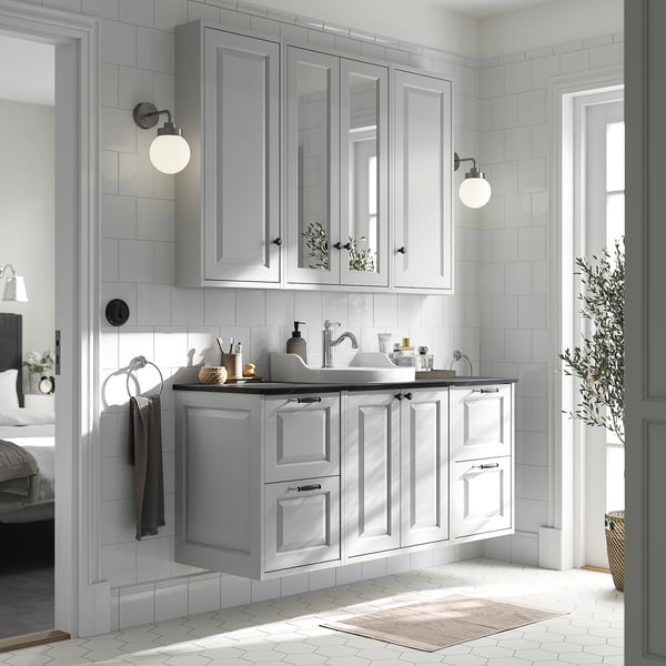 Modern bathroom with light grey TÄNNFORSEN cabinet set, marble counter, wall lamps, and plant.