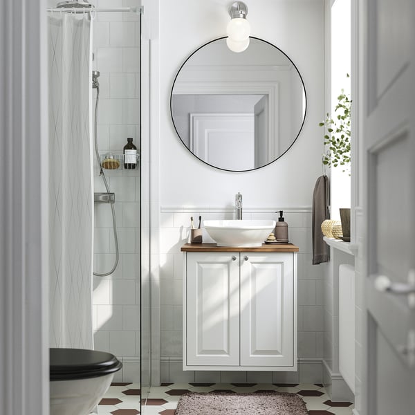 Modern minimalist bathroom: white TÄNNFORSEN vanity, round mirror, shower with glass door, dark hex tiles.