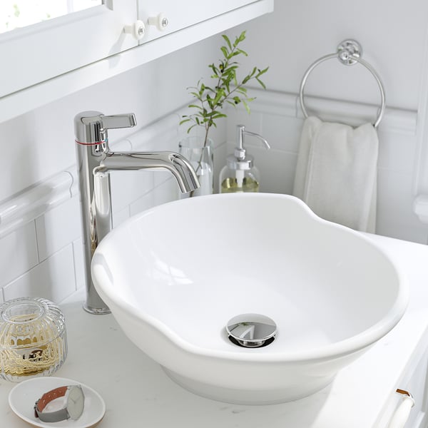 Modern bathroom sink with chrome tap, round basin, and towel ring. White countertop with decor items.