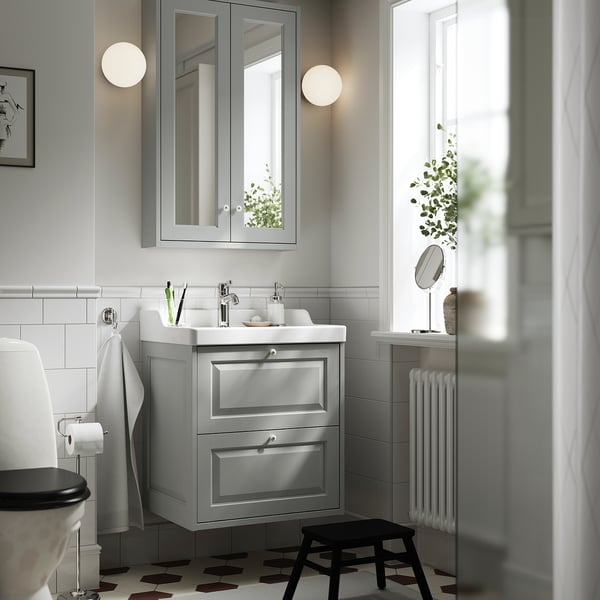 Modern grey bathroom with TÄNNFORSEN vanity, large mirror, white tiles, patterned floor, plants & radiator. Compact yet functional.