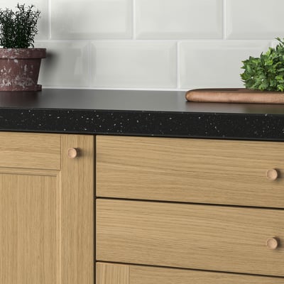 Wooden cabinet drawers with black speckled countertop, white tiled backsplash and potted herbs.