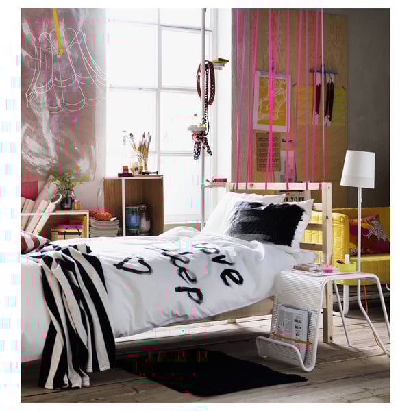 Modern bedroom with white TARVA bed, black & white linens, striped blanket, colourful decor, wide windows, shelves, and a desk by the window.