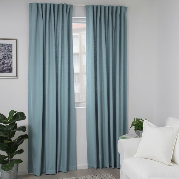 Blue TIBAST curtains hang near a white chair, providing privacy and reducing glare. Cotton fabric with polyester heading tape, offering a neat look.