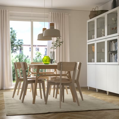 Modern dining room with beige rug, wooden table, chairs, and large windows.