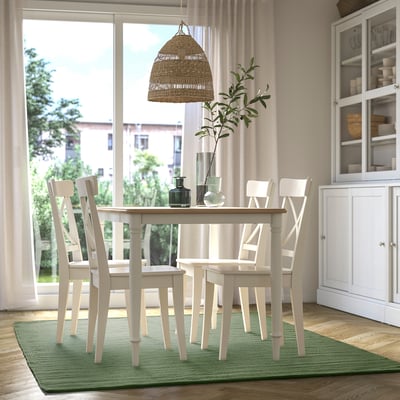 Modern dining room with TIDTABELL green rug, white chairs, wooden table, and woven pendant light.