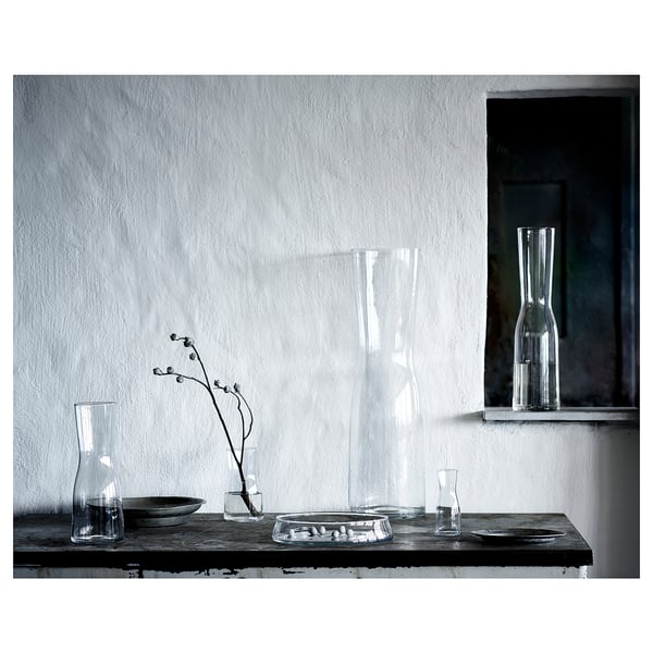 Clear glass vase with flowers on rustic table, white wall background.