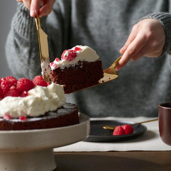 Person serving a slice of cake with a TILLAGD server from a plate, adding elegance to the table setting.