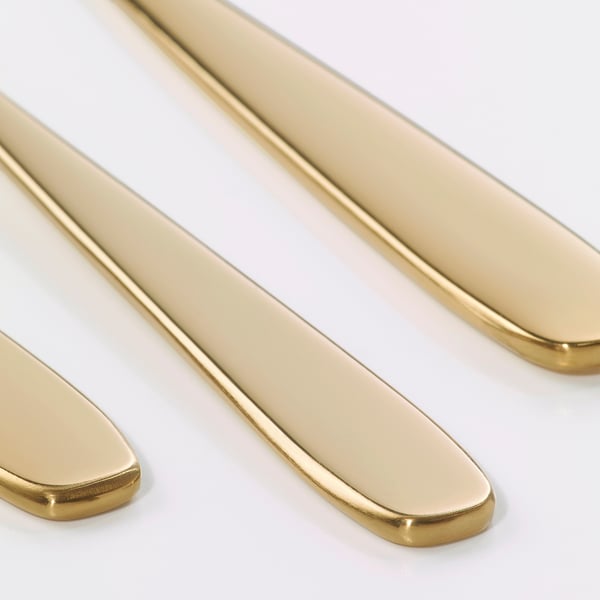 Waterfall of gleaming gold cutlery, polished, sleek, and sophisticated, arranged artfully against a pure white backdrop.