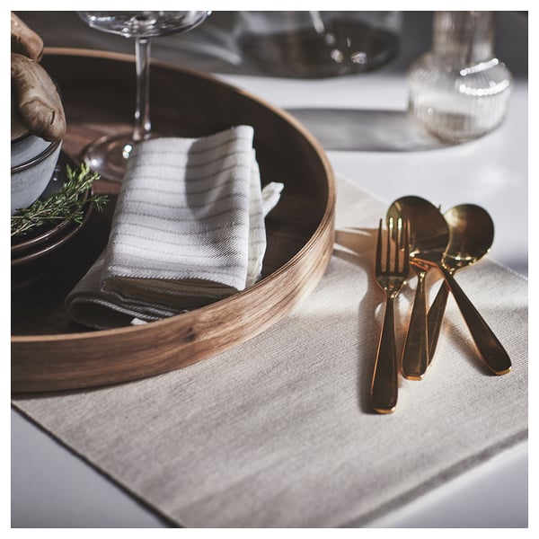 Elegant table setting with TILLAGD brass-colored cutlery and rustic wooden tray on light-colored placemat.